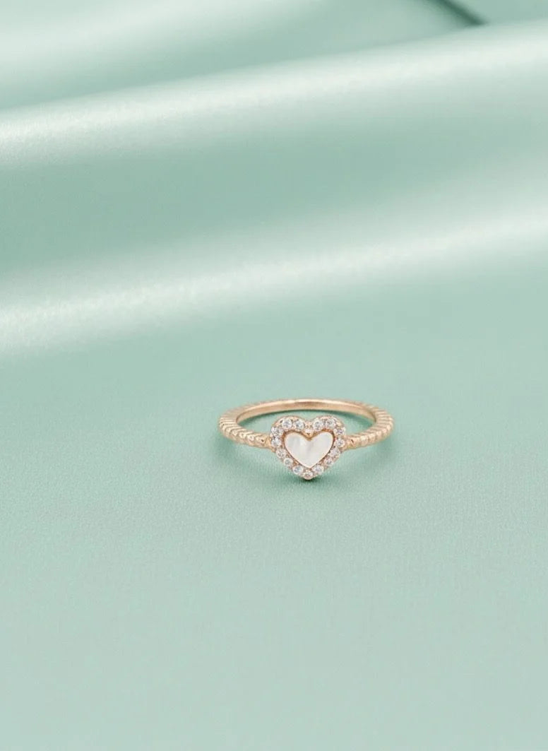 Rose gold ring with a heart-shaped center on a light green background