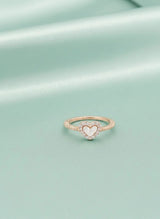 Rose gold ring with a heart-shaped center on a light green background