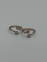 Two rose gold toe rings with gemstones on a light gray background