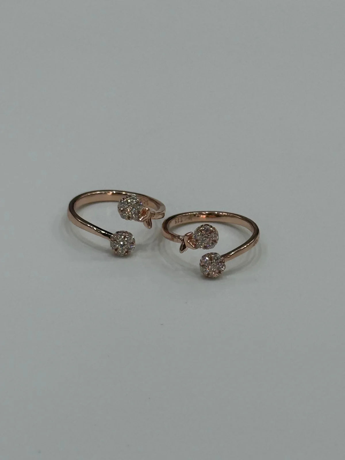 Two rose gold toe rings with gemstones on a light gray background