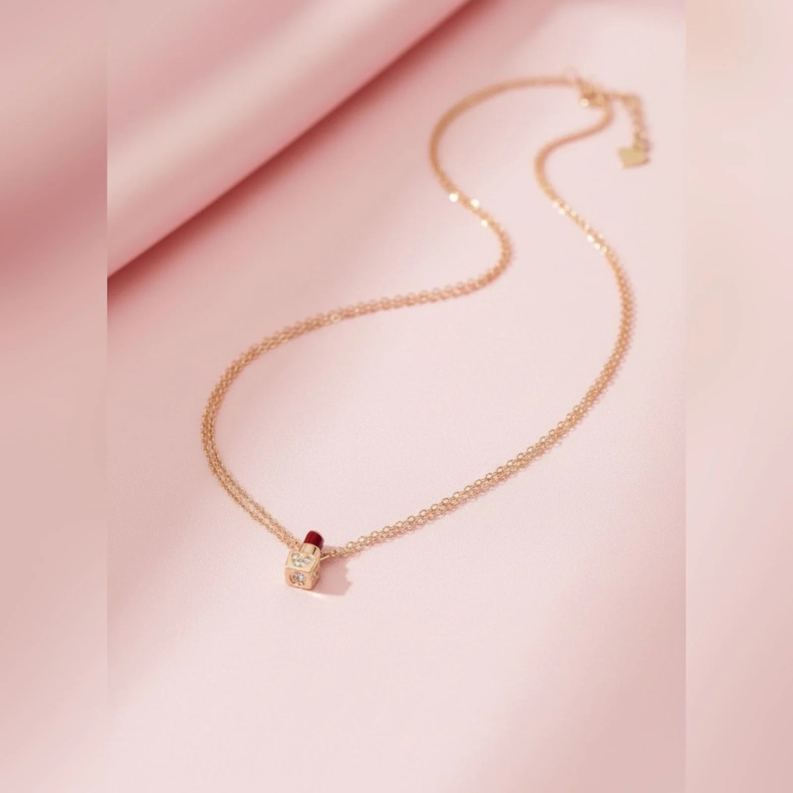 Rose gold necklace with a lipstick pendant on a pink fabric background