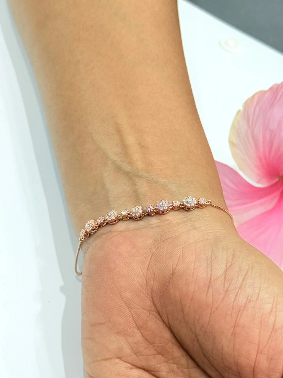 Rose gold bracelet with small stones on a wrist, blurred pink flower in the background
