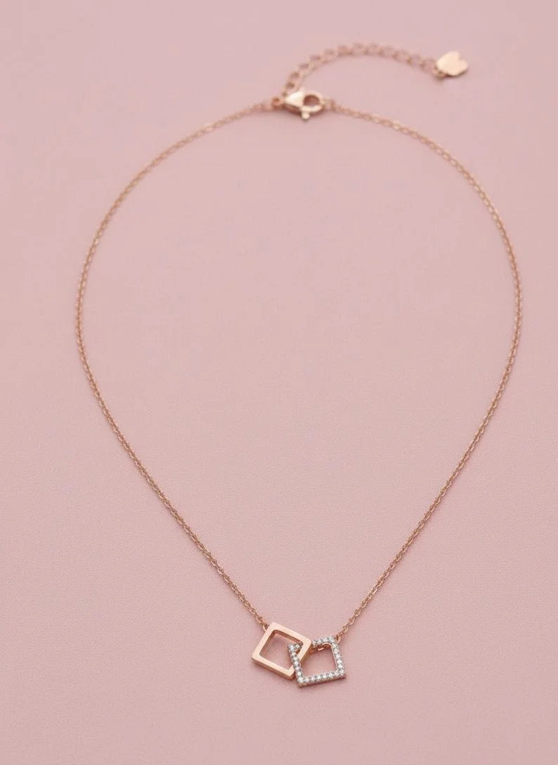 Rose gold necklace with interlocking square pendants on a pink background