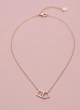 Rose gold necklace with interlocking square pendants on a pink background