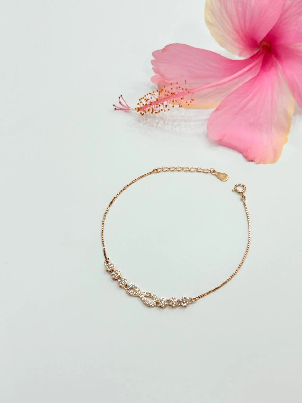 Gold bracelet on a light gray background with a pink flower.