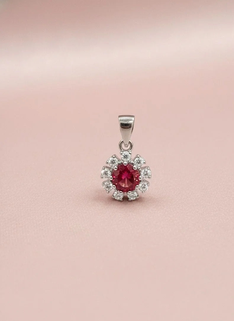 Silver pendant with a red gemstone on a pink background
