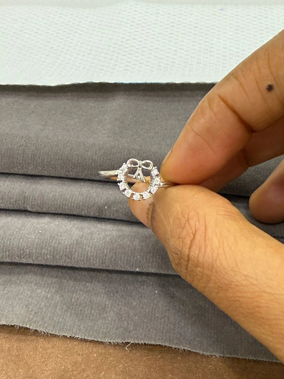 Silver ring with stones held between fingers on gray fabric