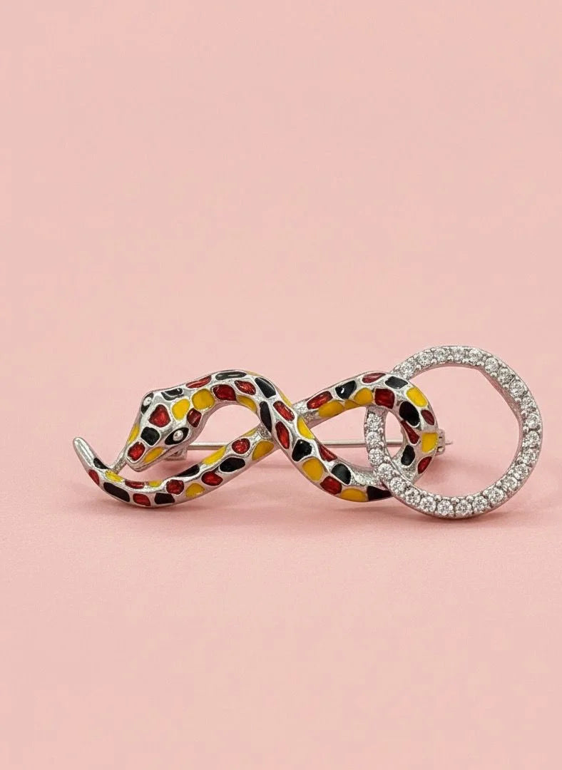 Pendants on a pink background, one snake-shaped with a colorful pattern and the other silver.