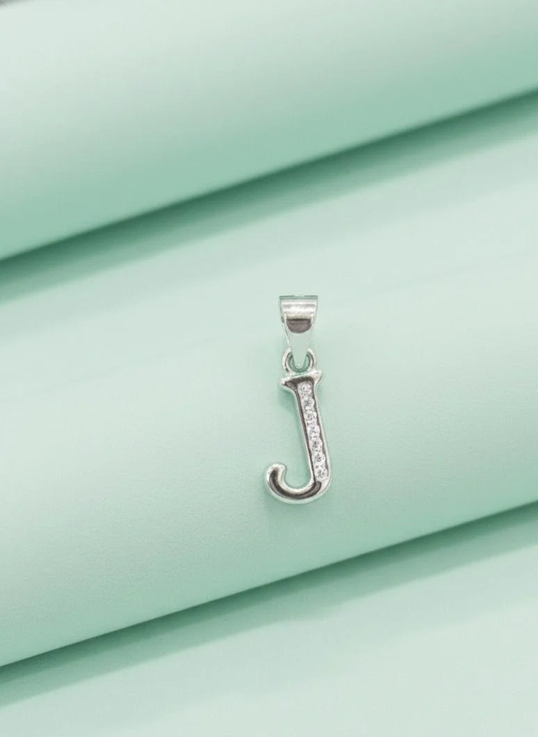 Silver pendant with a letter 'J' on a light green fabric background