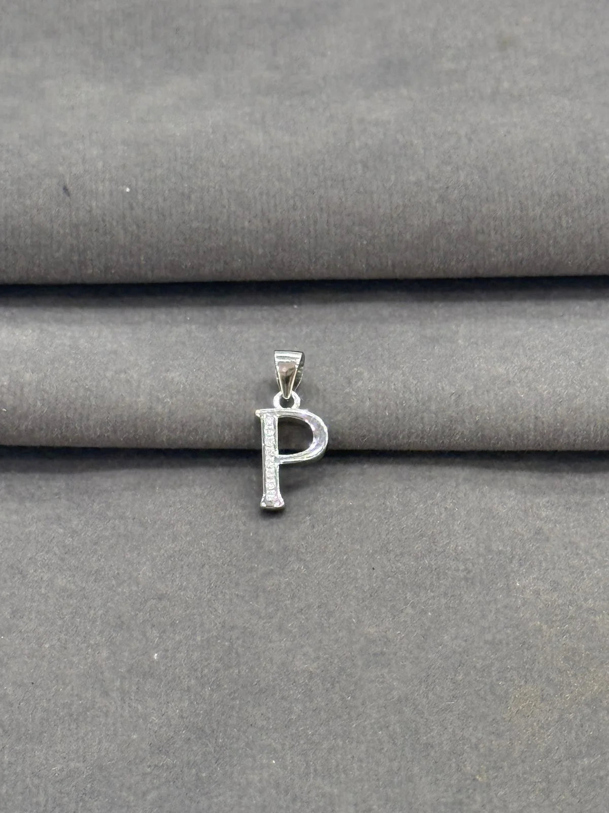 Silver 'P' pendant on a gray fabric background