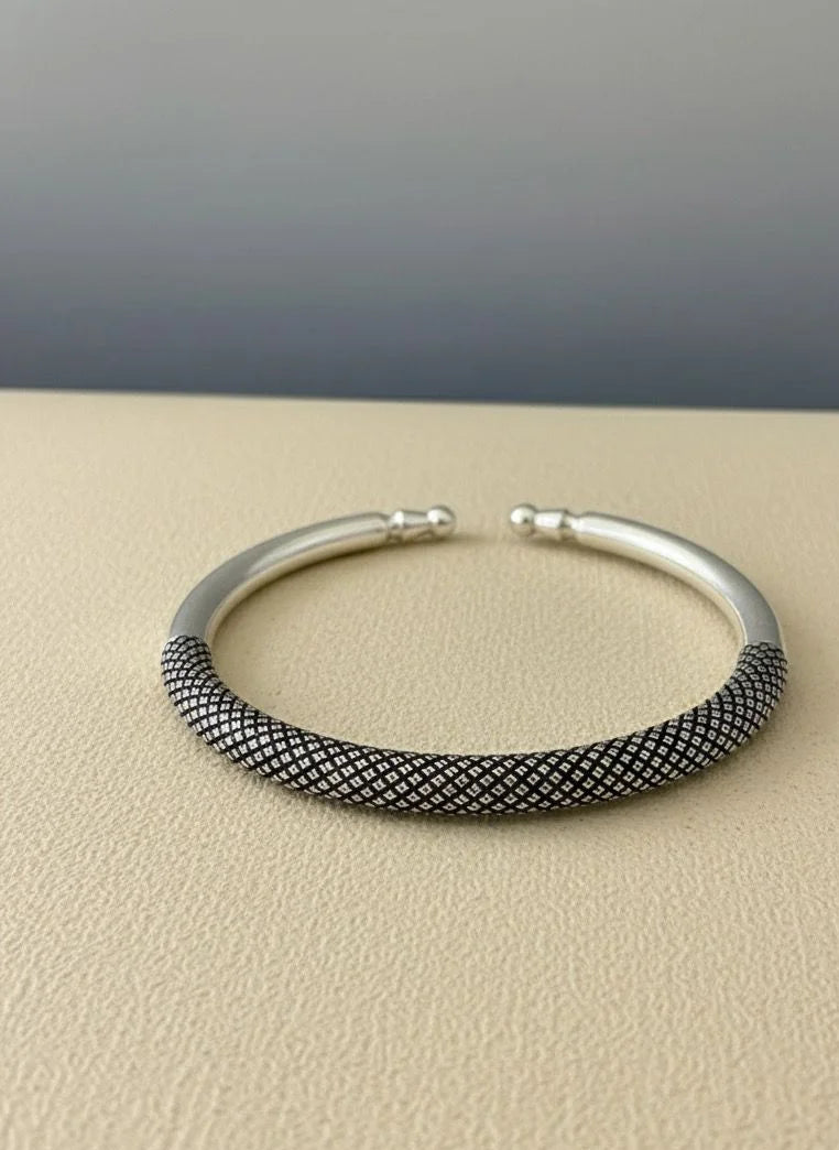 Silver bracelet with textured band on a beige surface
