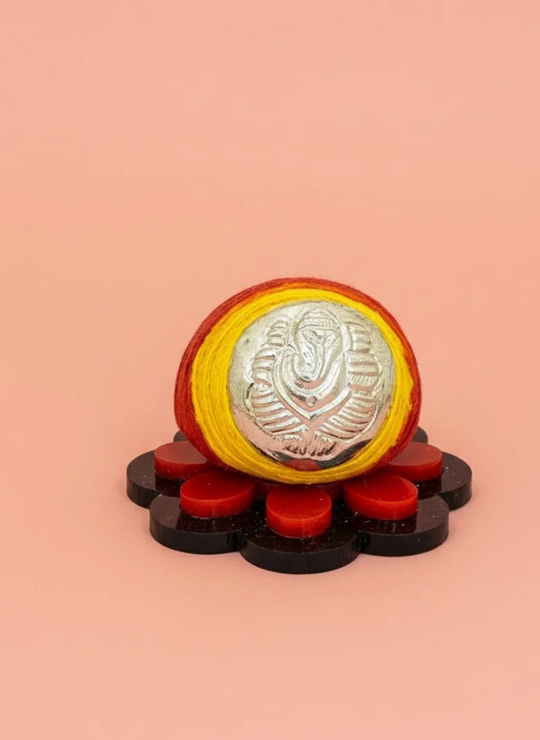 Decorative item with a central silver coin on a yellow background, surrounded by red and black elements on a peach background.