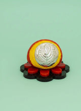 Decorative item with a central silver emblem, surrounded by red and black elements on a light green background