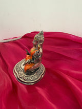 Statue of a seated figure on an ornate base with a pink fabric background