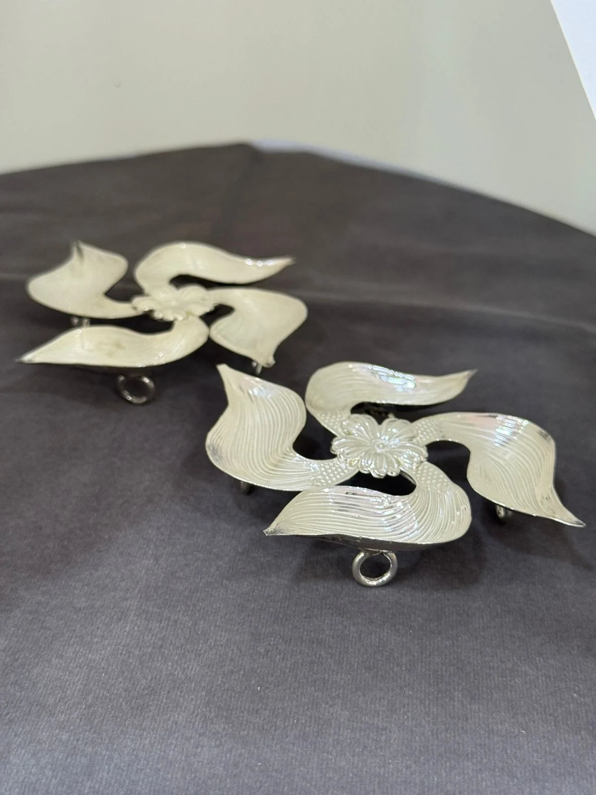 Pair of silver earrings with leaf-like designs on a gray surface.