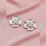 Pair of silver flower-shaped earrings on a pink fabric background