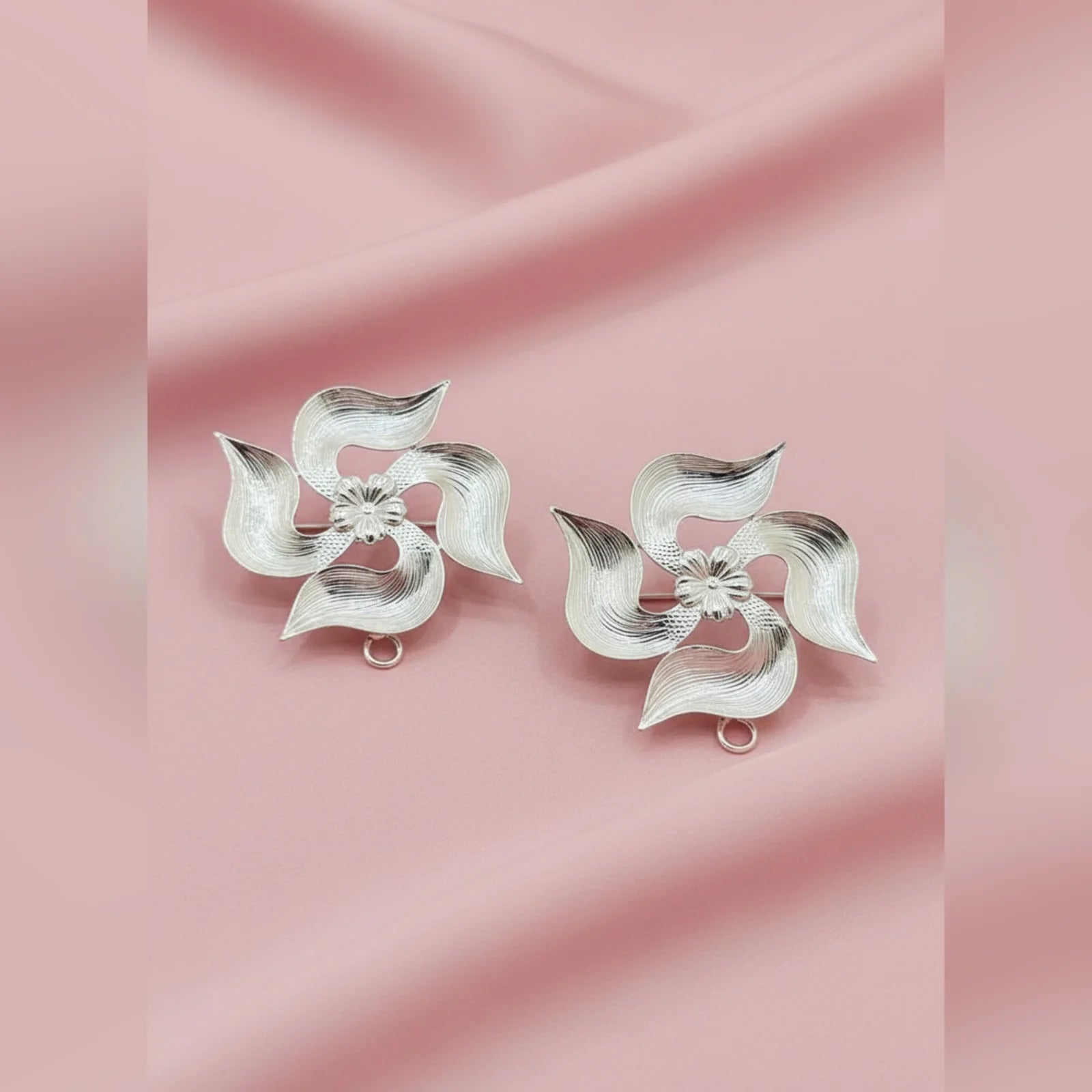 Pair of silver flower-shaped earrings on a pink fabric background