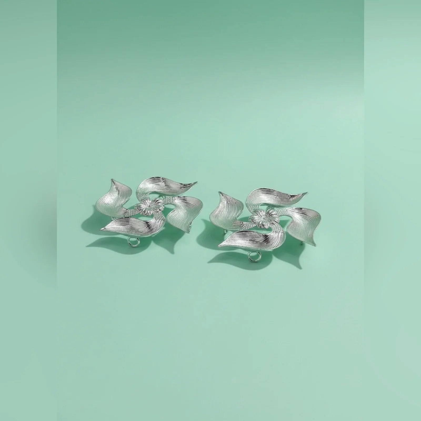Pair of silver leaf-shaped earrings on a light green background