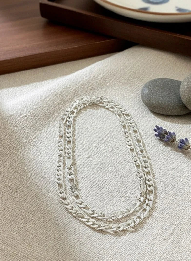 Silver chain necklace on a textured surface with stones and lavender flowers.