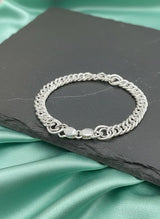 Silver chain bracelet on a dark slate surface with a green satin background
