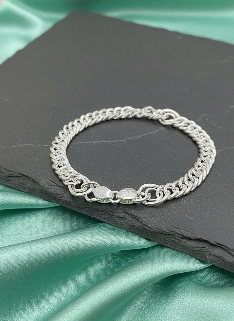 Silver chain bracelet on a dark slate surface with a green satin background