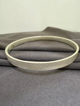 Gold tint bracelet with a textured band on a gray fabric background