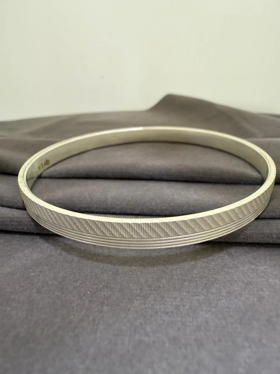 Gold tint bracelet with a textured band on a gray fabric background