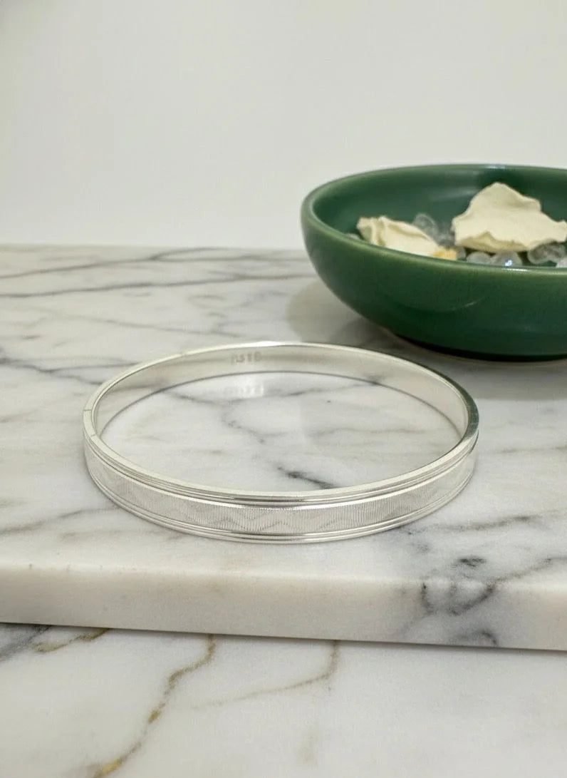 Silver bracelet on a marble surface with a green bowl in the background