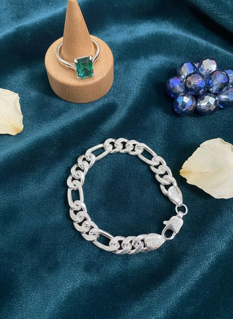 Silver bracelet on a blue satin surface with gemstones and a ring.