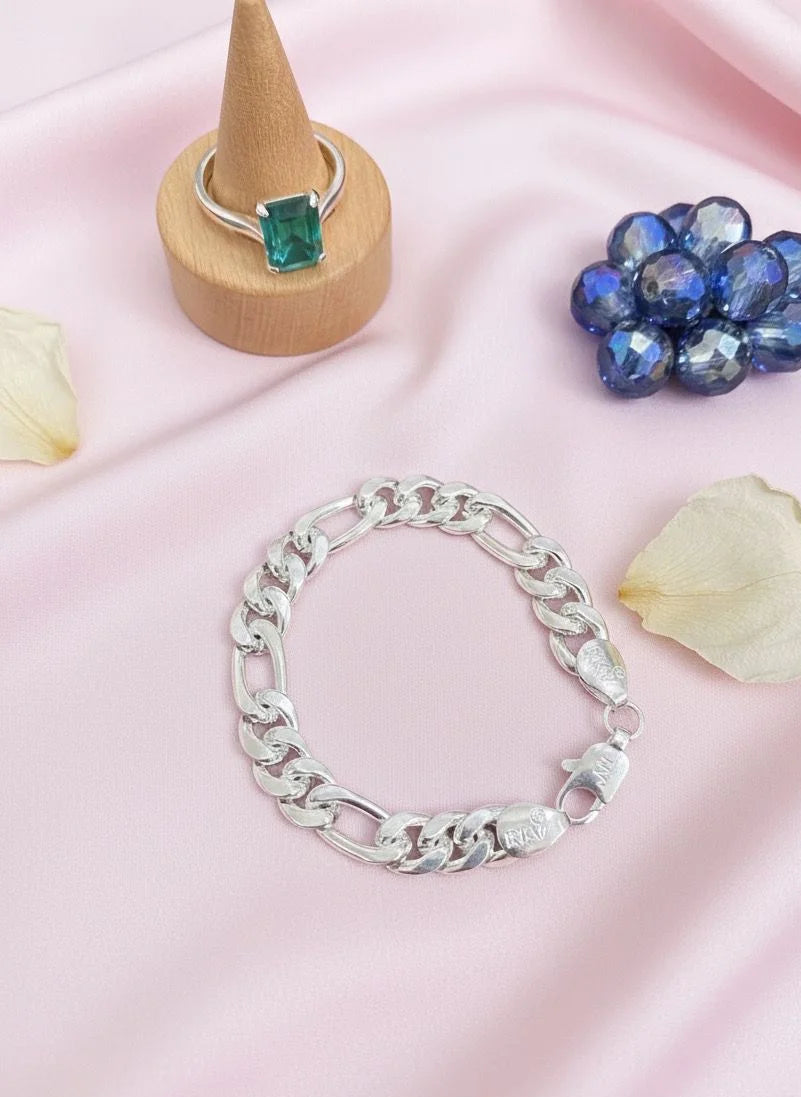 Silver bracelet on a pink fabric background with a ring and flower petals.