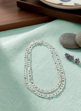 Silver chain necklace on a light green fabric surface with stones and lavender.
