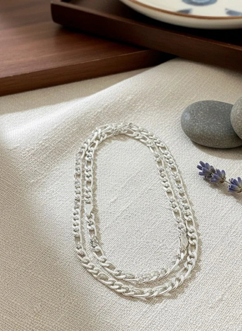 Silver chain necklace on a textured surface with stones and lavender flowers.
