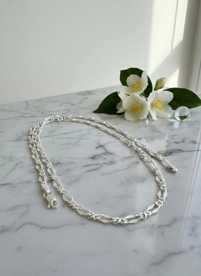 Silver chain necklace on a marble surface with white flowers