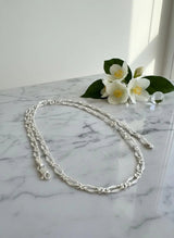 Silver chain necklace on a marble surface with white flowers