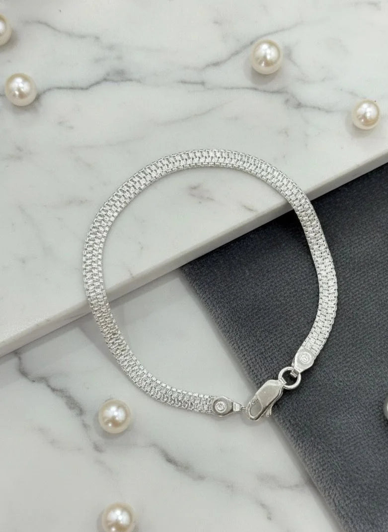 Silver bracelet on a marble surface with scattered pearls