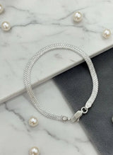 Silver bracelet on a marble surface with scattered pearls