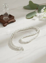 Silver necklace on a light surface with a glass bottle and greenery in the background