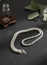 Silver necklace on a dark surface with green leaves and flowers in the background