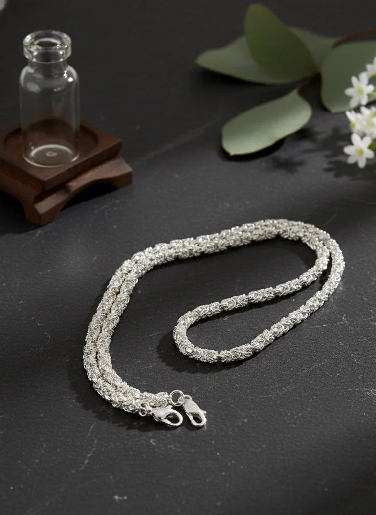 Silver necklace on a dark surface with green leaves and flowers in the background