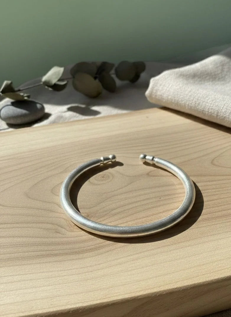 Silver bracelet on a wooden surface with stones and fabric in the background