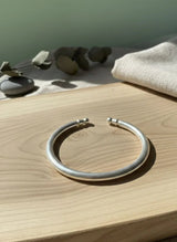 Silver bracelet on a wooden surface with stones and fabric in the background