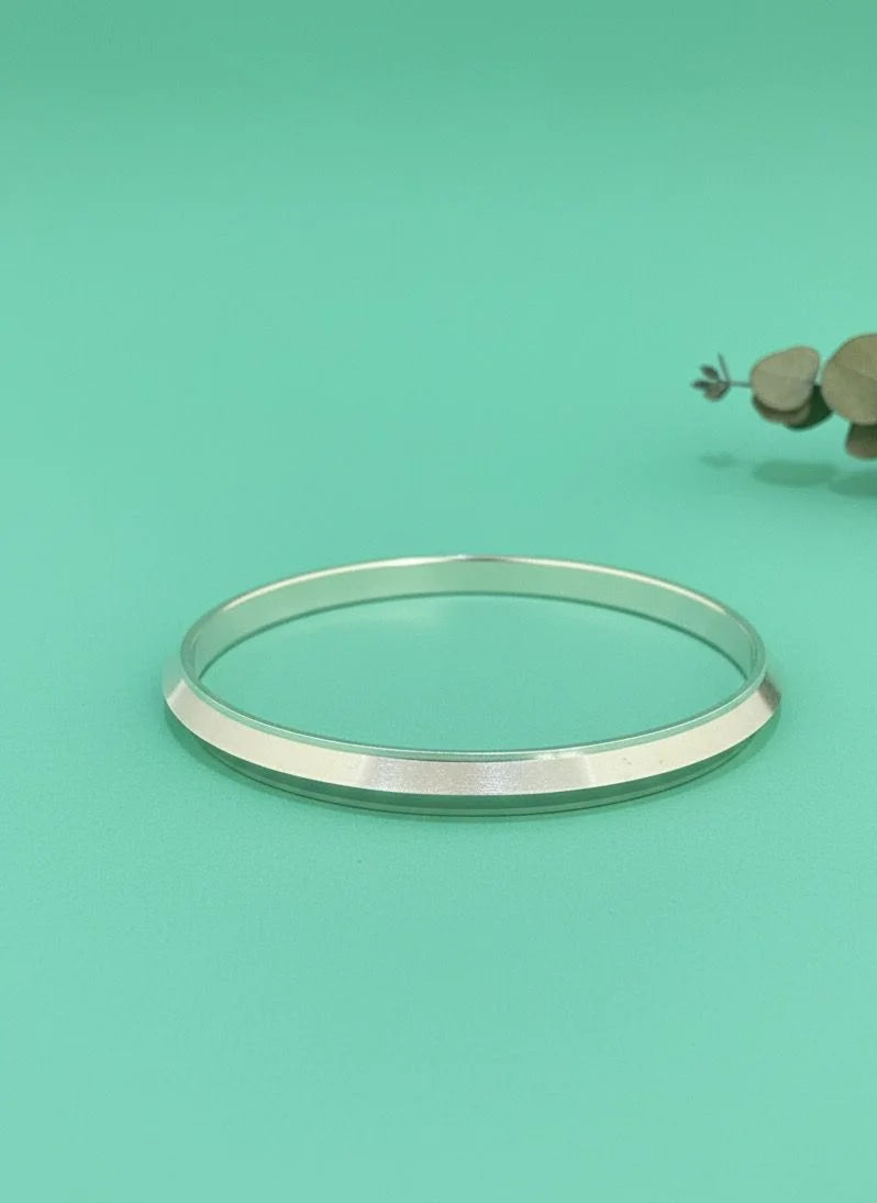Silver bangle on a teal background with a small branch of leaves.