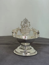 Silver decorative item with a central figure on a gray surface