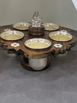 Decorative wooden table with silver bowls and a central statue on a gray surface.