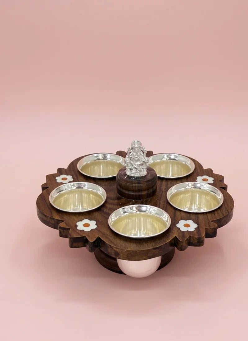 Wooden tray with silver bowls and a central decorative item on a pink background