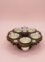 Wooden tray with silver bowls and a central decorative item on a pink background