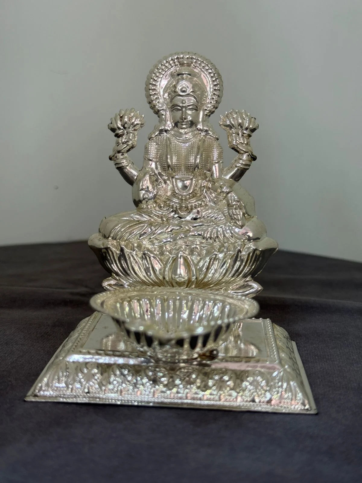 Silver deity statue on a reflective base against a plain background