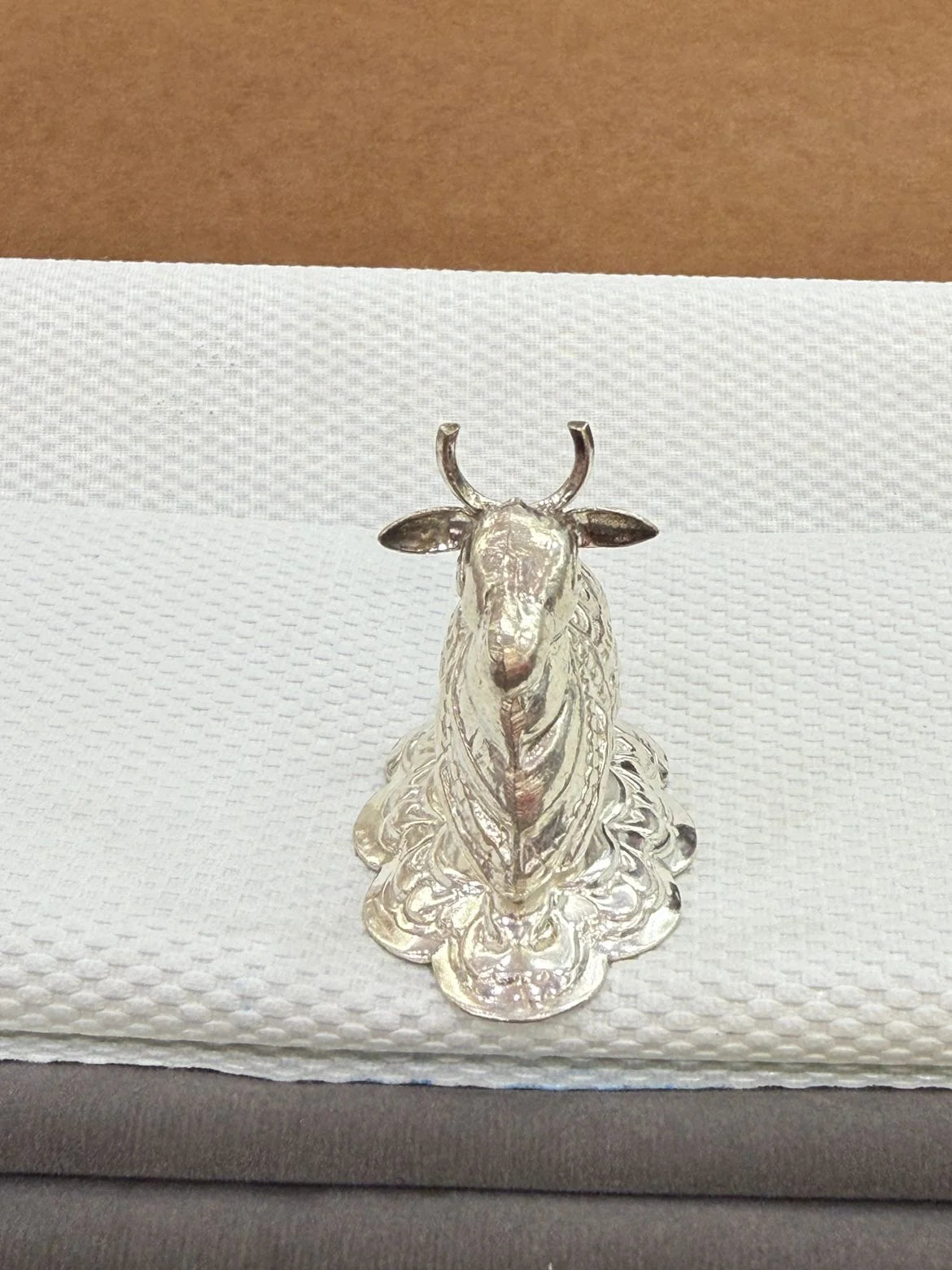 Silver cow figurine on a textured white surface with a brown background