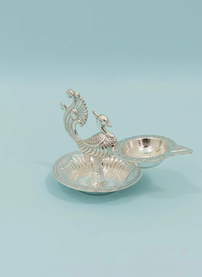 Decorative silver peacock-shaped oil lamp on a light blue background