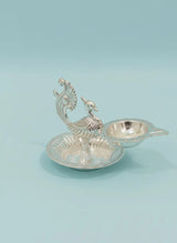 Decorative silver peacock-shaped oil lamp on a light blue background
